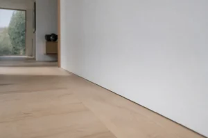 Plinthe affleurante invisible entre parquet chêne et mur blanc dans intérieur contemporain