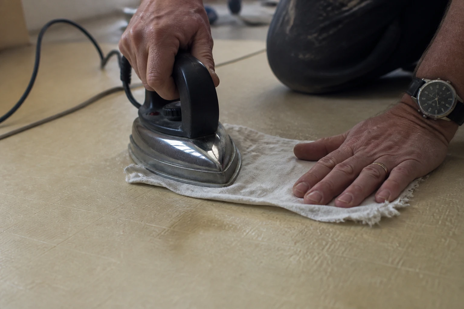 Réparation d'un lino enfoncé au fer à repasser et chiffon humide sur un sol beige