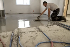Artisan appliquant une chape de ravoirage sur un sol béton avec canalisations apparentes